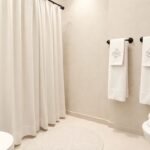 Μπάνιο με όμορφη υφασμάτινη κουρτίνα, ομοιόμορφες πετσέτες, διακοσμητικό σαπούνι και στυλάτο χαλάκι.