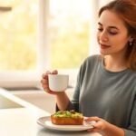 Μια γυναίκα απολαμβάνει ένα υγιεινό πρωινό με αβοκάντο και καφέ σε μια ηλιόλουστη κουζίνα.