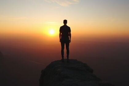 Ένας άνθρωπος κοιτάζει το ηλιοβασίλεμα από ένα βράχο, συμβολίζοντας την ανασκόπηση και την ελπίδα για τη νέα χρονιά.