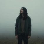 Μοναχική φιγούρα σε ομιχλώδη τοπίο, σκεπτική και μελαγχολική.