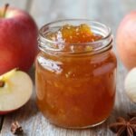 Σπιτική αρωματική μαρμελάδα μήλου σε γυάλινο βάζο με φρέσκα μήλα και μπαχαρικά γύρω της.