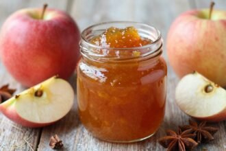 Σπιτική αρωματική μαρμελάδα μήλου σε γυάλινο βάζο με φρέσκα μήλα και μπαχαρικά γύρω της.