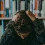 A child appears stressed and frustrated while seated in a library, holding their head.