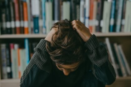 A child appears stressed and frustrated while seated in a library, holding their head.