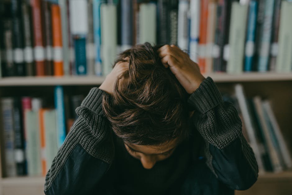 A child appears stressed and frustrated while seated in a library, holding their head.
