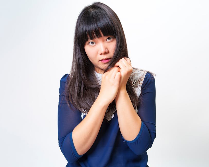 Τα 4 κουρέματα του 2026 που ταιριάζουν σχεδόν σε κάθε πρόσωπο 4 Portrait of a contemplative Asian woman holding her hair in front of a white background.