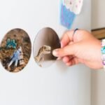 A child's hand with bracelets holding a dinosaur magnet on a refrigerator adorned with stickers.