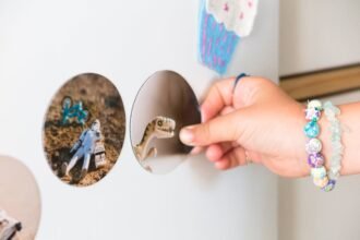 A child's hand with bracelets holding a dinosaur magnet on a refrigerator adorned with stickers.