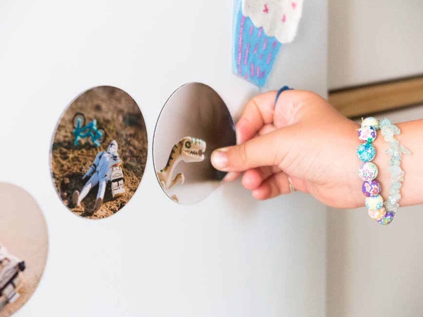 A child's hand with bracelets holding a dinosaur magnet on a refrigerator adorned with stickers.