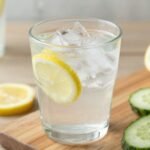 Ένα γυάλινο ποτήρι με νερό γεμάτο πάγο και φέτες λεμονιού και αγγουριού.