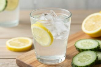 Ένα γυάλινο ποτήρι με νερό γεμάτο πάγο και φέτες λεμονιού και αγγουριού.