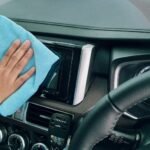 Close-up of a hand cleaning a car dashboard with a blue microfiber cloth.