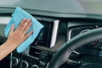Close-up of a hand cleaning a car dashboard with a blue microfiber cloth.