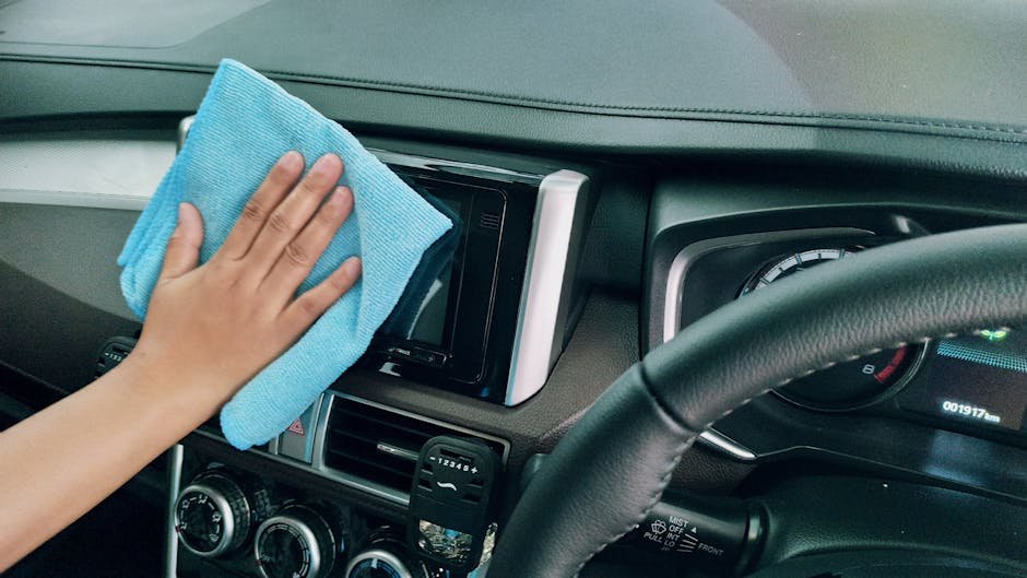 Close-up of a hand cleaning a car dashboard with a blue microfiber cloth.
