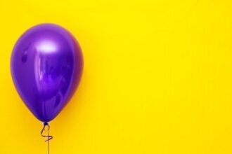 A single purple balloon with a vivid yellow backdrop, creating a bold contrast.