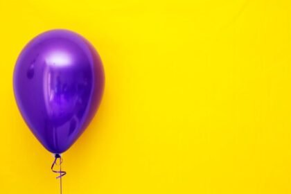 A single purple balloon with a vivid yellow backdrop, creating a bold contrast.