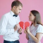 Couple holding broken heart halves on pink background
