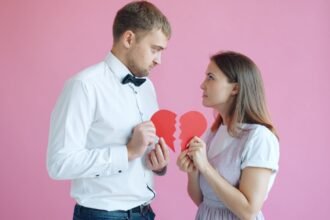 Couple holding broken heart halves on pink background