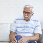 Ηλικιωμένος άνδρας στο σπίτι του που αγγίζει το πονεμένο γόνατό του