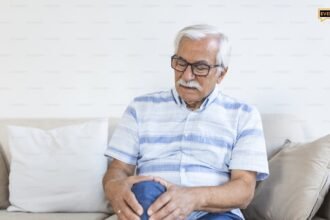 Ηλικιωμένος άνδρας στο σπίτι του που αγγίζει το πονεμένο γόνατό του