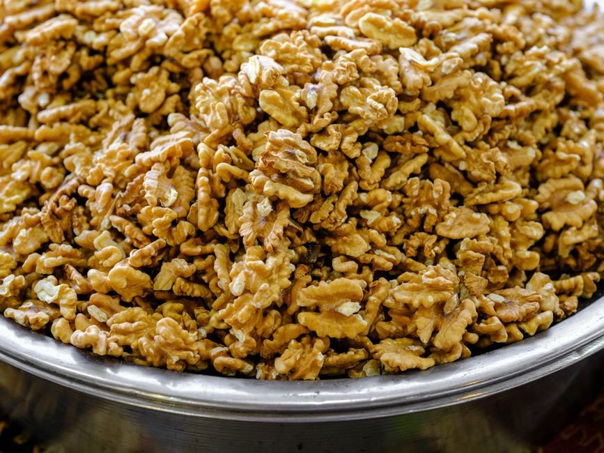 Close-up of a large number of walnuts piled in a metal bowl, showcasing their texture.