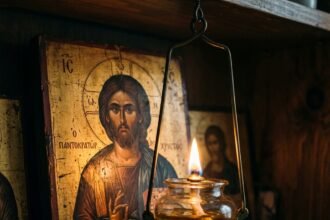 Κοντινό πλάνο σε ένα αναμμένο καντήλι που καίει μπροστά από την εικόνα του Χριστού