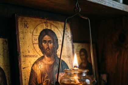 Κοντινό πλάνο σε ένα αναμμένο καντήλι που καίει μπροστά από την εικόνα του Χριστού