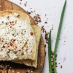 Top view of bread slices with cream cheese and spices on a wooden board.