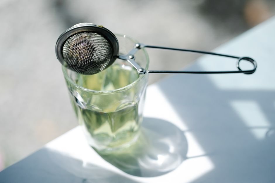 A tea strainer resting on a glass with sunlight casting shadows, creating a serene tea-making ambiance.