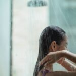 Side view of lady with closed eyes standing in shower and enjoying water