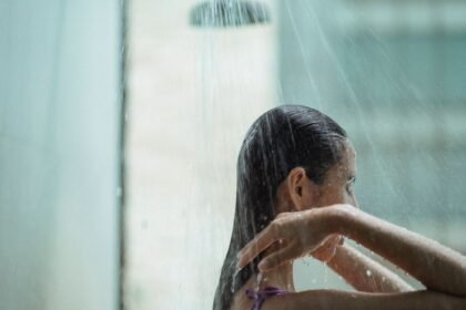 Side view of lady with closed eyes standing in shower and enjoying water