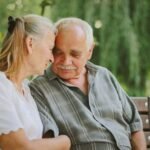 Elderly couple sitting closely, enjoying a joyful moment together in a serene outdoor setting.