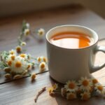 Μια ζεστή κούπα με ρόφημα χαμομηλιού σε ένα ξύλινο τραπέζι με αποξηραμένα άνθη δίπλα της