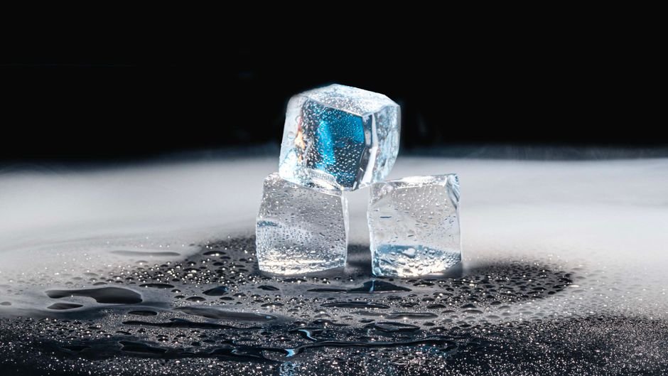 Three ice cubes melting on a black surface with water droplets.